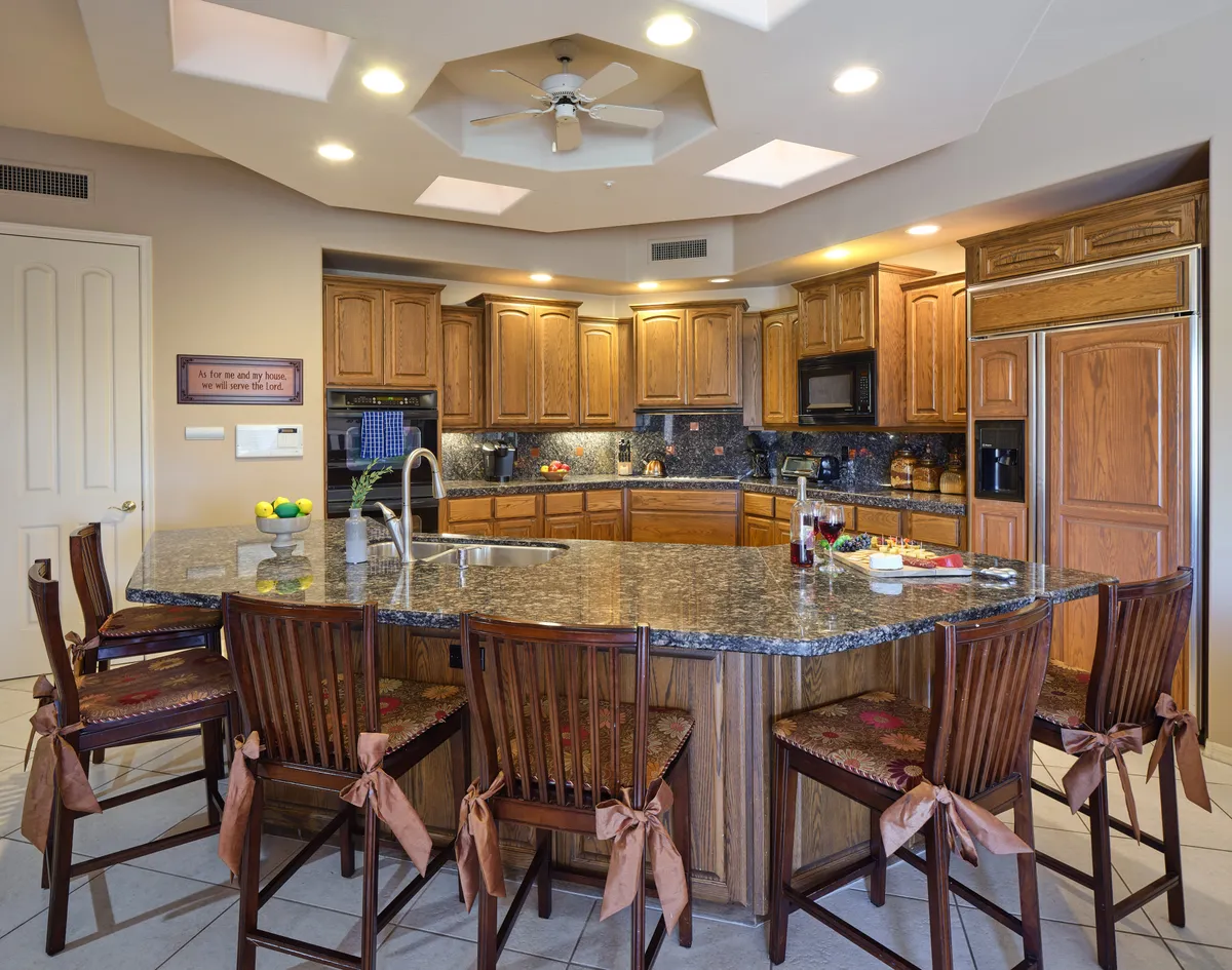 A warm kitchen environment with a granite island, wooden cabinets, a seating area, and a decorative fruit bowl. The kitchen opens into the living spaces, making it ideal for both preparing meals and socializing with guests.