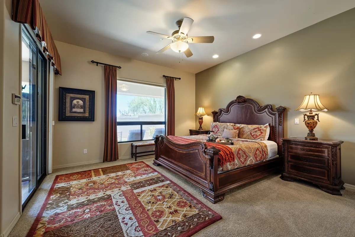A cozy bedroom featuring an ornate wooden bed, topped with intricate bedding, flanked by stylish lamps and set on a decorative rug. Warm, soft lighting creates an inviting atmosphere, and the space is clearly designed for relaxation and comfort.