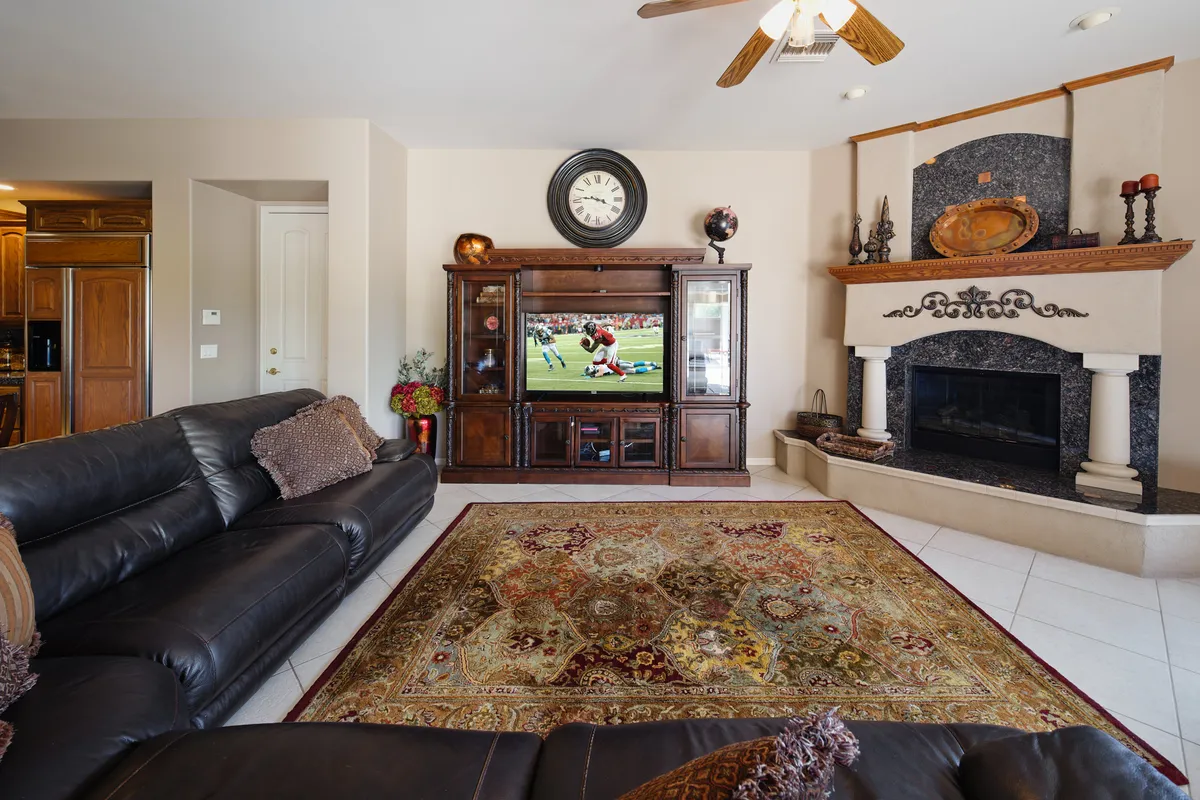 A cozy family room featuring plush leather sofas, an ornate area rug, an entertainment center with a Smart TV, and a glowing fireplace as the focal point. The space is arranged for both relaxing and social gatherings, inviting guests to unwind, watch movies, or enjoy conversations by the fire.