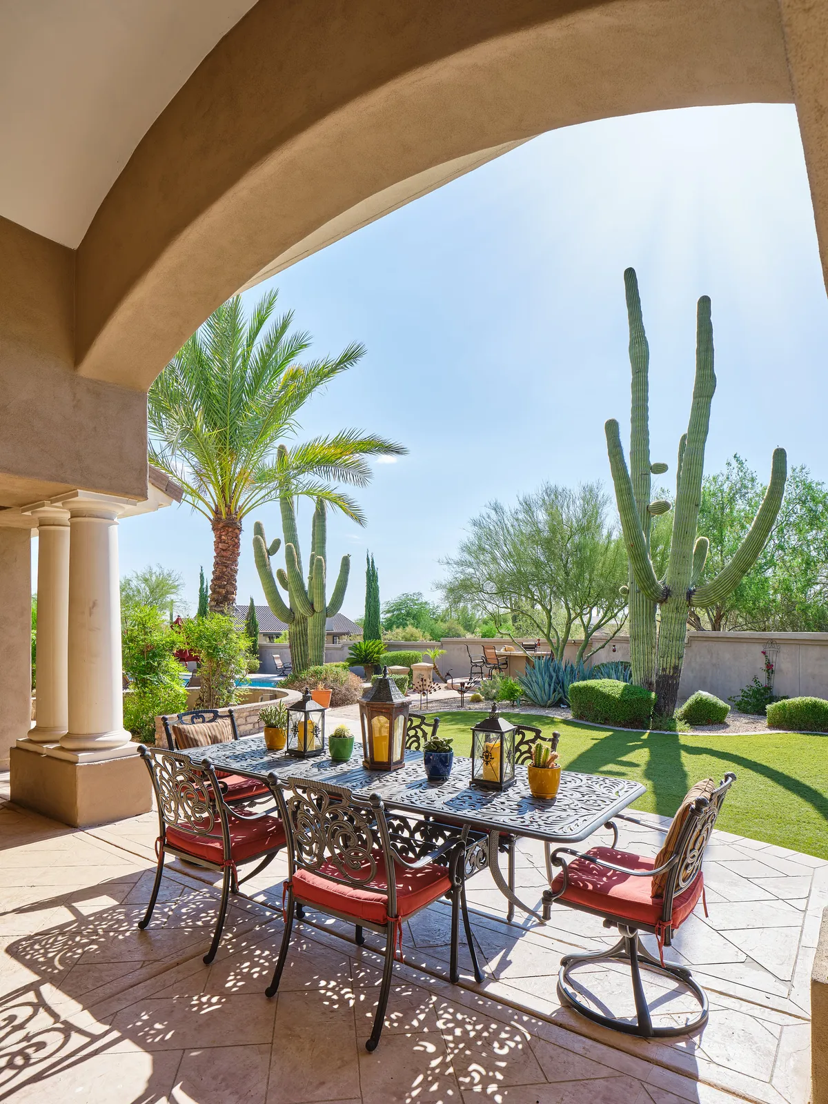 An exterior shot featuring a beautifully set outdoor dining table surrounded by lush greenery, tall cacti, and palm trees. The relaxed, cheerful ambiance invites guests to dine al fresco, entertain, or simply enjoy the Arizona sunset in a resort-style setting.
