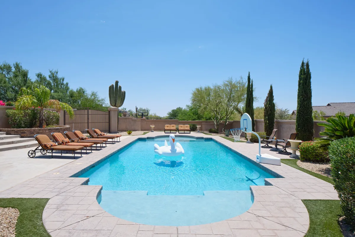An inviting exterior shot of the villa’s backyard, showcasing a sparkling swimming pool, sun-drenched lounge chairs, cacti, and a basketball hoop at the poolside. The cheerful scene hints at fun-filled afternoons spent swimming, playing, and relaxing together after a day of exploring nearby attractions.