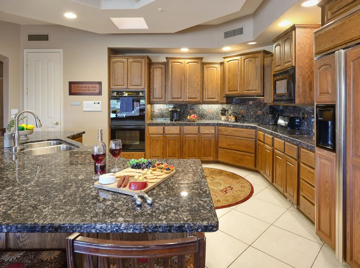 A close-up view of a granite countertop adorned with a food platter and wine glasses, surrounded by wooden cabinets. The scene suggests a moment of entertaining and enjoying good company, with a focus on meal sharing and hospitality.